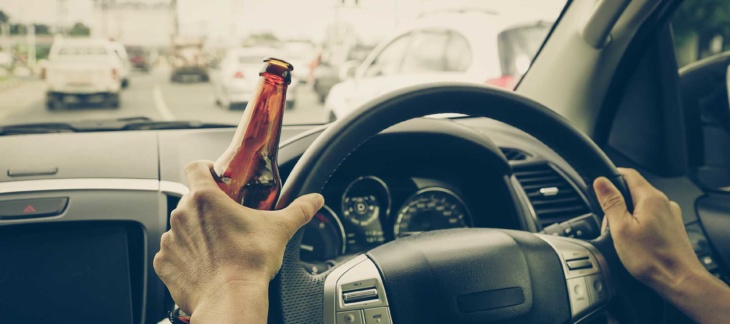 Driver holding alcoholic bottle while driving on busy road during the day