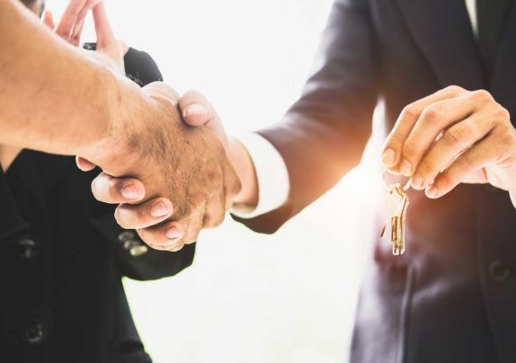 Two men shaking hands, with man in suit also holding keys in other hand