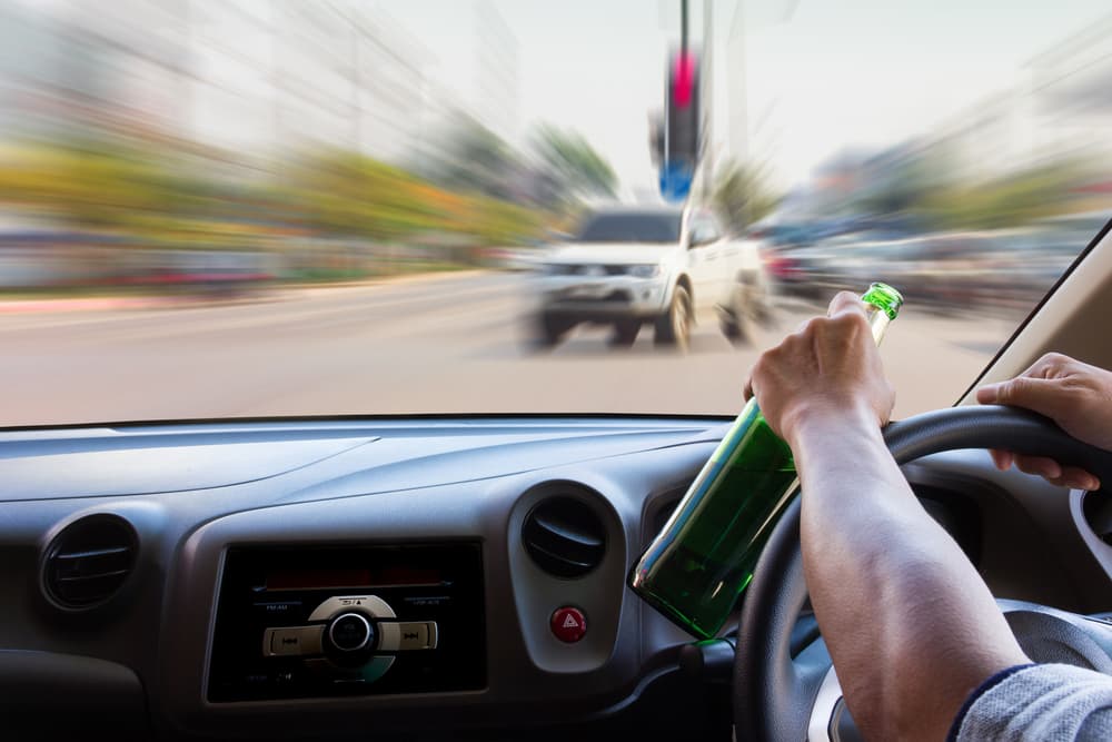 A drunk man driving a car with a bottle of alcohol in the front seat