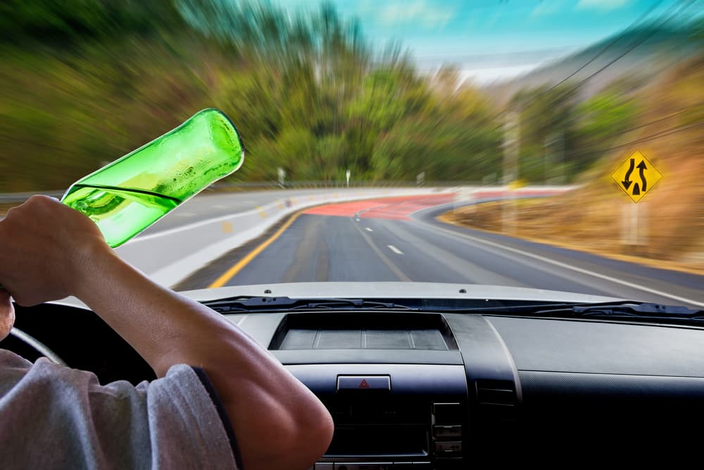 A drunk person driving a car with a green bottle placed on the window sill