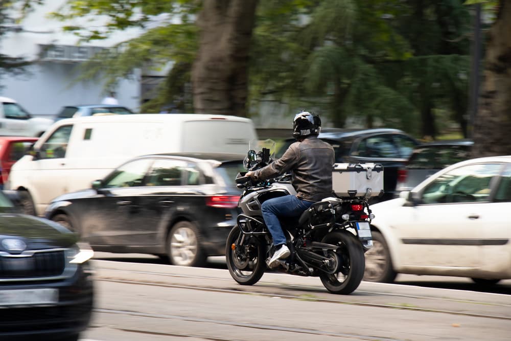 Man riding a motorbike in busy city street traffic on tram track, from behind