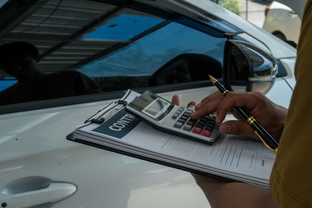 Person reviewing documents and using a calculator beside a car, representing car accident settlement calculation.