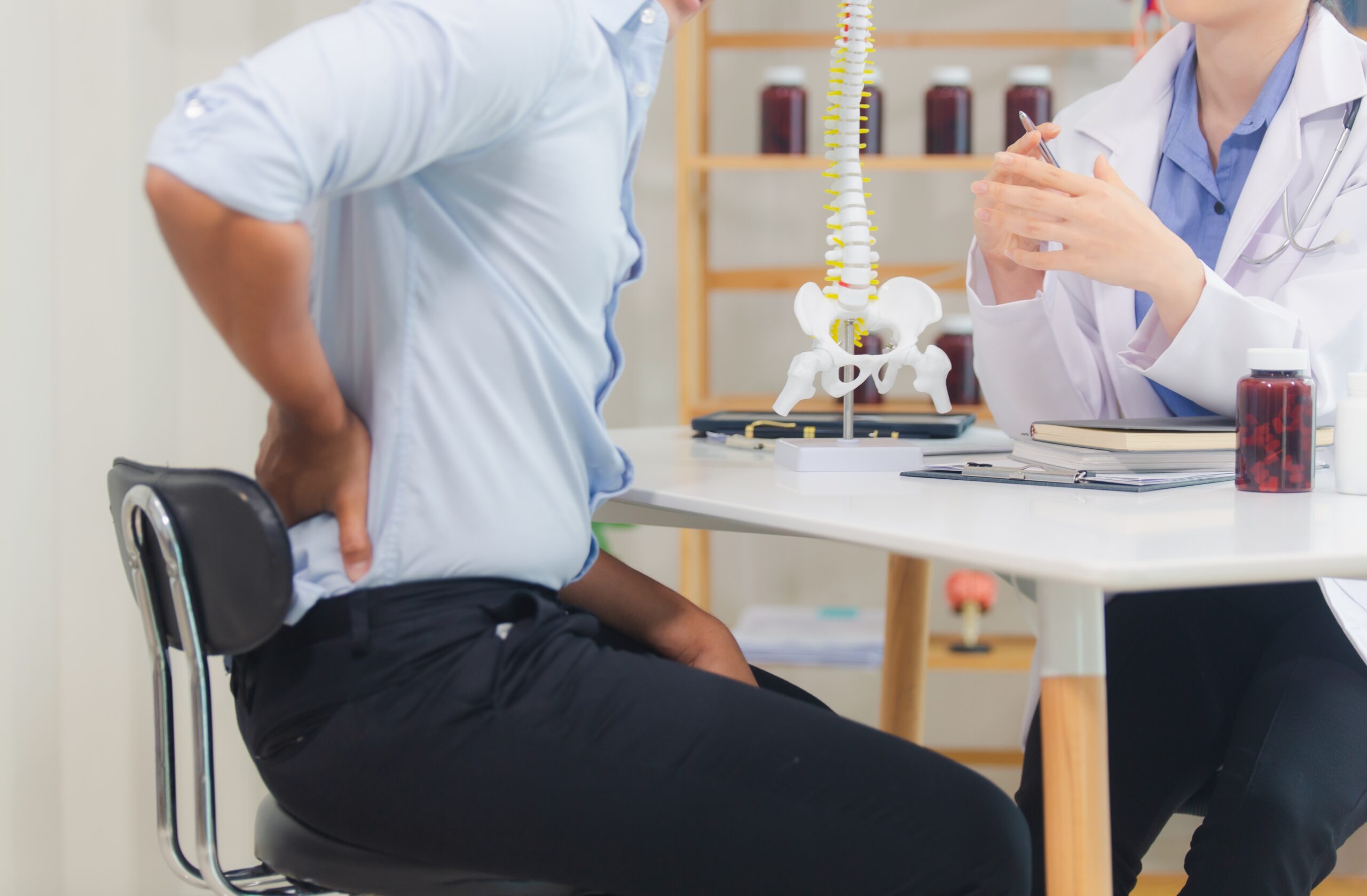 Patient holding their lower back in pain while consulting with a medical professional in an exam room