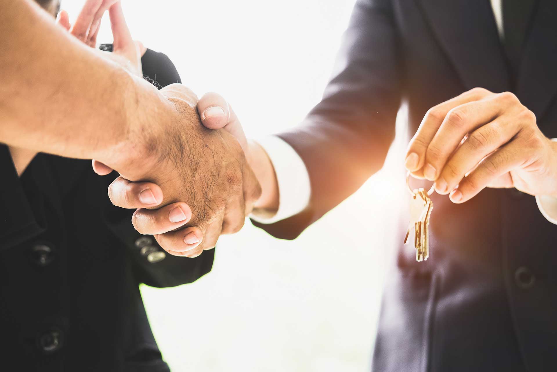 Two individuals shaking hands while one person holds a set of house keys