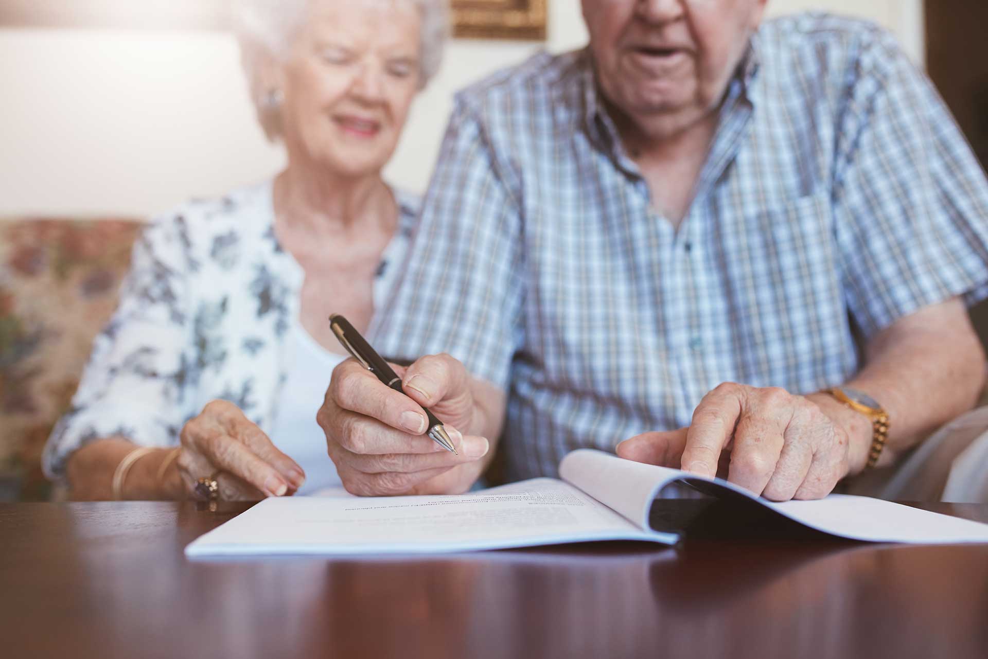 Elderly couple reviewing and signing legal documents together at a table in their home