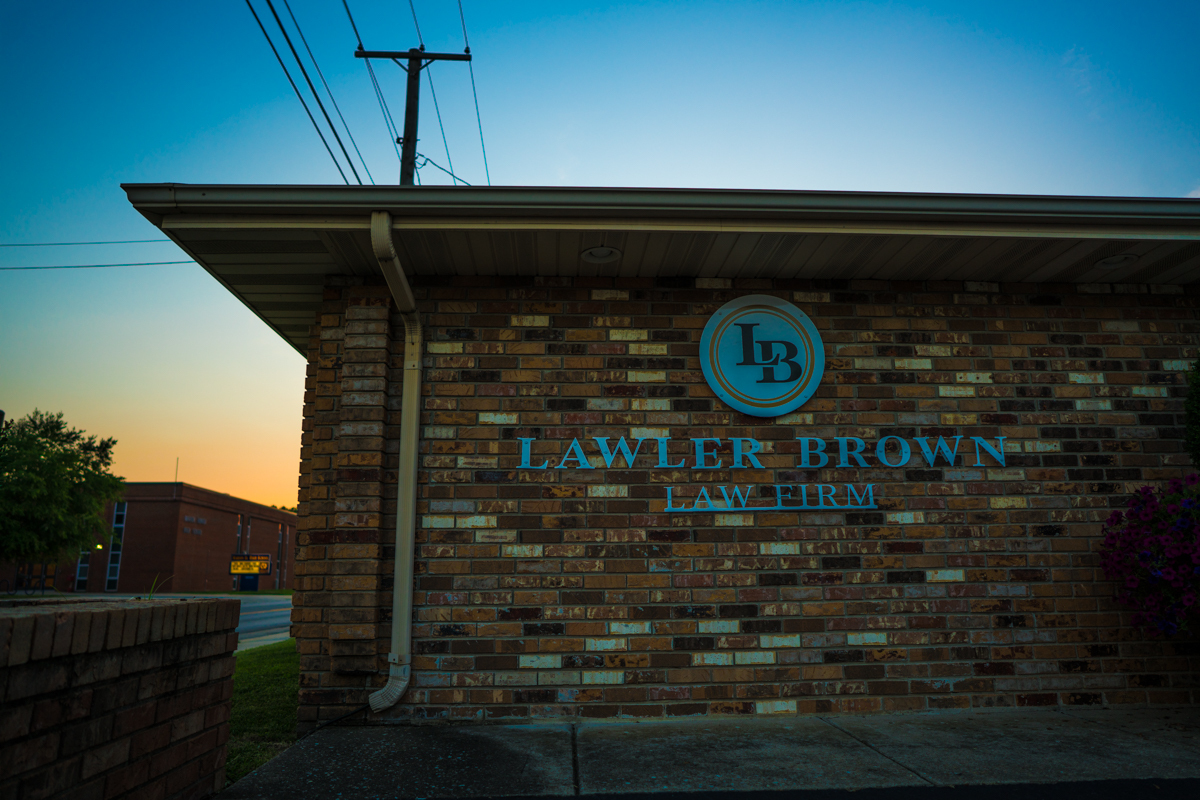 Exterior view of the Lawler Brown Law Firm office building featuring the firm’s name and logo mounted on a brick wall at sunset