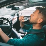 Man drinking alcohol while seated behind the wheel of a car