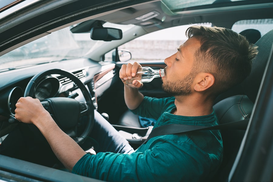 Man drinking alcohol while seated behind the wheel of a car